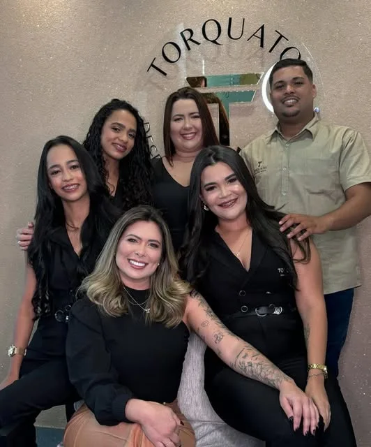 Equipe da Torquato Despachante no escritório da Iputinga, em frente ao letreiro TORQUATO na parede.